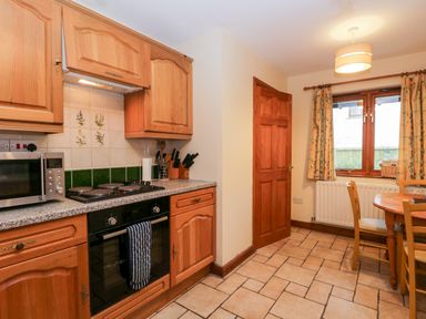 A kitchen with wooden cabinets a stove microwave a dining table and chairs at Friars Fold in Newby Bridge