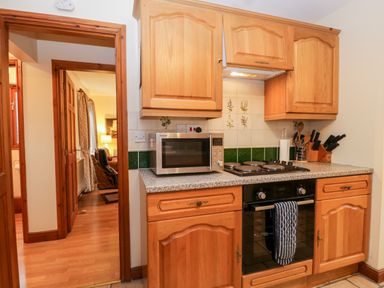 A kitchen with wooden cabinets a microwave oven a stovetop and kitchen utensils at Friars Fold in Newby Bridge
