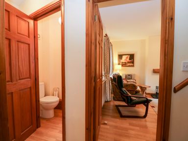 A hallway with wooden doors leading to a bathroom with a toilet and a living room with chairs and a lamp at Friars Fold in Newby Bridge