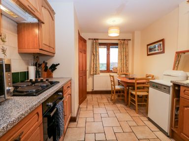 A kitchen with wooden cabinets a stove oven washing machine and a dining table with chairs at Friars Fold in Newby Bridge