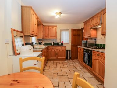 A kitchen with wooden cabinets a countertop microwave oven and a wooden table with chairs at Friars Fold in Newby Bridge