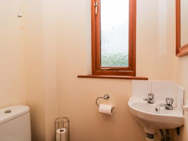 A small bathroom with a toilet sink a window and toilet paper at Friars Fold in Newby Bridge