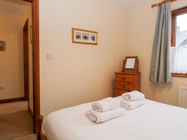 A bedroom with a bed with folded towels a wooden chest of drawers with a mirror and a window with curtains at Friars Fold in Newby Bridge