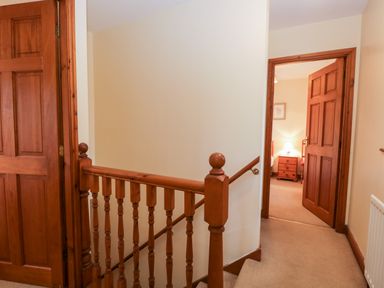 A hallway with wooden doors and a railing leading to a bedroom with a nightstand and lamp at Friars Fold in Newby Bridge