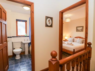 A hallway with a wooden railing showing a bathroom with a toilet and sink and a bedroom with a bed and bedside table at Friars Fold in Newby Bridge