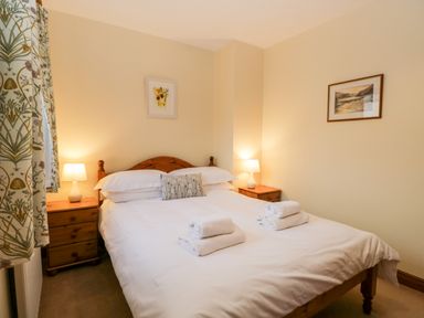 A bedroom with a double bed two bedside tables with lamps and folded towels on the bed at Friars Fold in Newby Bridge