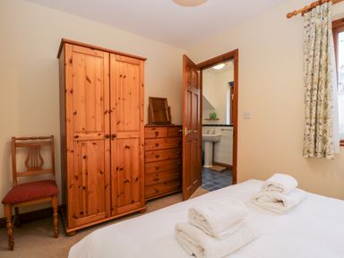 A bedroom with a wooden wardrobe dresser chair and a bed with folded towels next to a door leading to a bathroom at Friars Fold in Newby Bridge