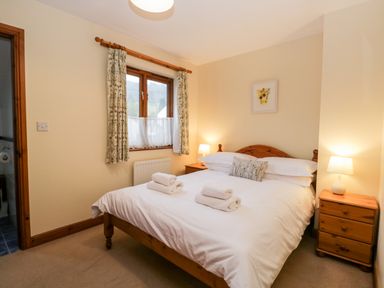 A bedroom with a double bed, bedside tables with lamps, a window with curtains, and folded towels on the bed at Friars Fold in Newby Bridge