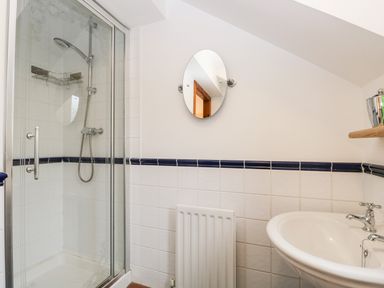 A bathroom with a glass shower enclosure a white sink a small round mirror and a radiator at Friars Fold in Newby Bridge