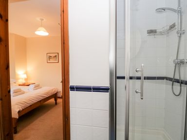 A bedroom with a wooden bed and nightstand next to a tiled bathroom with a shower at Friars Fold in Newby Bridge
