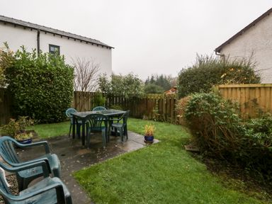A backyard with green plastic chairs and table on a paved area surrounded by grass and shrubs at Friars Fold in Newby Bridge