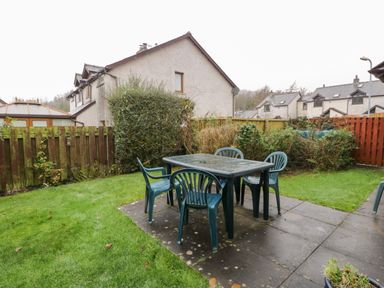 A garden with a patio table and plastic chairs surrounded by grass and bushes at Friars Fold in Newby Bridge