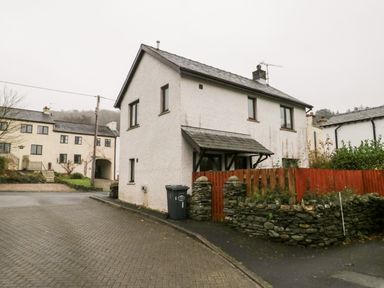 A two-story house with a small porch and a red wooden fence next to a stone wall at Friars Fold in Newby Bridge