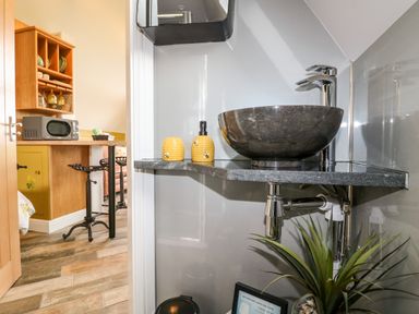 A bathroom corner with a stone sink and yellow soap dispensers near a kitchen counter with bar stools at Buttercup Lodge in Misterton