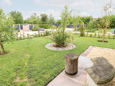 A garden with a circular plant bed and a wooden stool next to a stone bench at Buttercup Lodge in Misterton