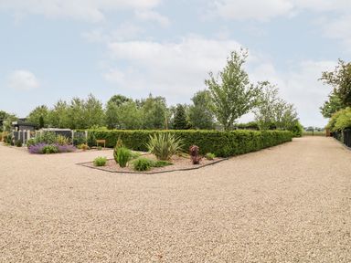 A gravel driveway with landscaped garden beds and hedges at Buttercup Lodge in Misterton