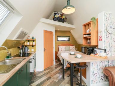A compact loft room with a kitchen area a small dining counter a bed and floral wallpaper at Buttercup Lodge in Misterton