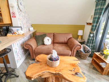 A sitting area with a brown leather sofa wooden coffee table and a side table with a lamp at Buttercup Lodge in Misterton