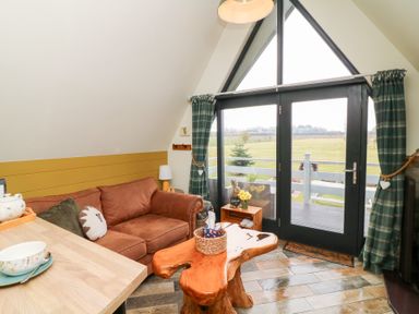 A living room with a brown sofa wooden coffee table and glass doors opening to a balcony at Buttercup Lodge in Misterton