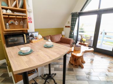 A small living area with a wooden table set with bowls and plates a brown sofa a coffee table and large windows at Buttercup Lodge in Misterton