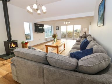 A living room with a large sofa a wooden coffee table a fireplace and a wall-mounted television at Yr Hen Feudy in Moelfre
