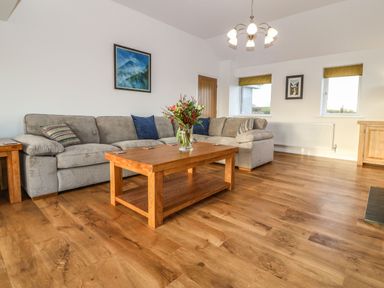 A living room with a gray corner sofa and wooden coffee table with flowers at Yr Hen Feudy Moelfre