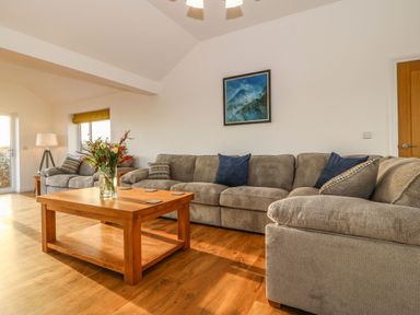 A living room with a wooden coffee table and a beige sofa set with cushions at Yr Hen Feudy in Moelfre