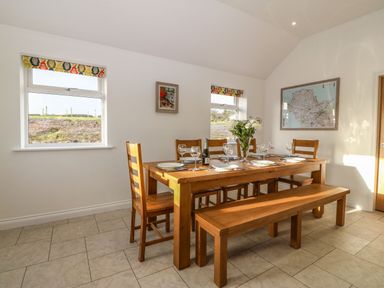 A dining area with a wooden table set with plates glasses and cutlery and surrounded by chairs and a bench at Yr Hen Feudy in Moelfre