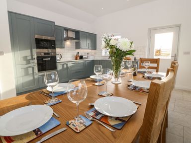 A wooden dining table set with plates wine glasses and cutlery in a kitchen with green cabinets and white tiled walls at Yr Hen Feudy in Moelfre
