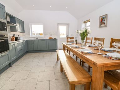 A kitchen with green cabinets and a wooden dining table set up with plates and glasses at Yr Hen Feudy in Moelfre