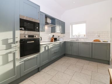 A kitchen with built in oven and microwave gray cabinets white countertops and a window at Yr Hen Feudy in Moelfre
