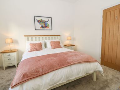 A bedroom with a bed two bedside tables lamps a colorful cow painting and a wooden door at Yr Hen Feudy in Moelfre