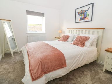 A bedroom with a bed with pink pillows and throw a standing mirror and bedside tables at Yr Hen Feudy in Moelfre