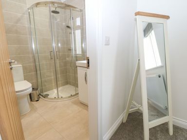 A bathroom with a shower, toilet, and sink next to a standing mirror in a white room at Yr Hen Feudy in Moelfre