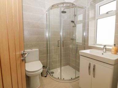 A bathroom with a toilet a corner shower enclosure and a sink with cabinet at Yr Hen Feudy in Moelfre