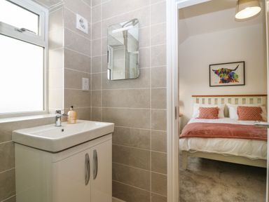 A bathroom with a sink and mirror next to a bedroom with a bed and colorful artwork at Yr Hen Feudy in Moelfre