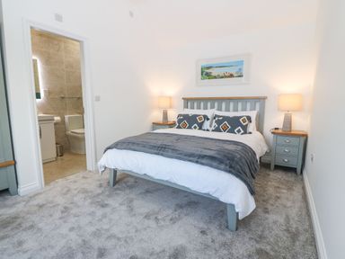 A bedroom with a bed pillows lamps on bedside tables and a bathroom beyond the open door at Yr Hen Feudy in Moelfre
