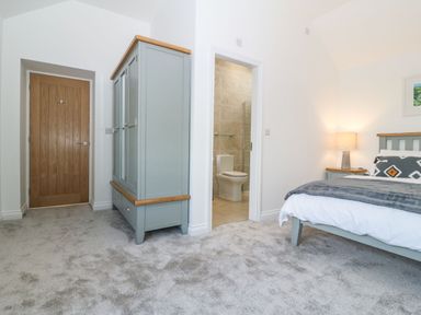 A bedroom with a bed and wardrobe next to a door leading to a bathroom at Yr Hen Feudy in Moelfre