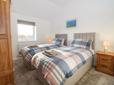 A bedroom with two single beds with plaid bedding beside a wooden nightstand and a window at Yr Hen Feudy in Moelfre