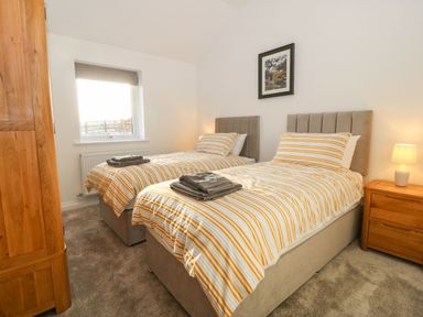 A bedroom with two single beds a wooden wardrobe bedside table and a lamp at Yr Hen Feudy in Moelfre