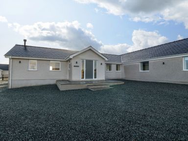 A single-story house with grey roof tiles and grey pebble ground at Yr Hen Feudy in Moelfre