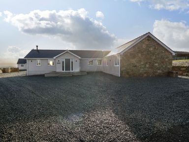 The exterior of a single-story house with a gravel driveway and a stone wall section at Yr Hen Feudy in Moelfre