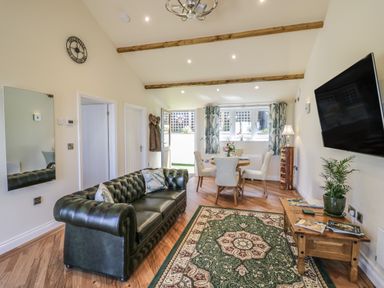 A living room with a green leather sofa wooden dining table with chairs a wall clock and a mounted television at FAIRFIELD in Clee Hill
