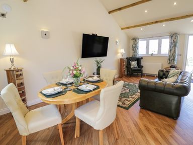A dining area with a round wooden table set for four and a living room with green leather sofas and a patterned rug at FAIRFIELD in Clee Hill