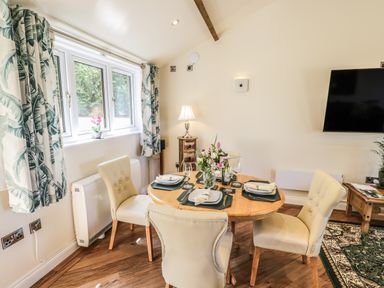 A dining area with a round wooden table set for four and cream chairs near a window with patterned curtains at FAIRFIELD in Clee Hill