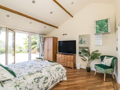 A bedroom with a bed floral bedding a wooden wardrobe a wooden dresser a television a green chair a plant and sliding glass doors at FAIRFIELD in Clee Hill