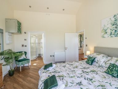 A bedroom with a bed and green floral bedding a chair with matching cushion a plant and an open door leading to a bathroom at FAIRFIELD in Clee Hill