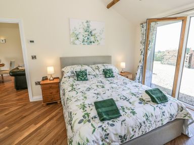 A bedroom with a double bed floral bedding bedside tables lamps and an open door to a patio at FAIRFIELD in Clee Hill