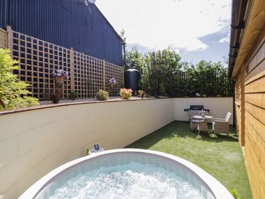 An outdoor space with a bubbling hot tub artificial grass a table with chairs a barbeque and a wooden fence at FAIRFIELD in Clee Hill