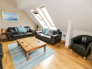 A living room with two dark leather sofas a wooden coffee table a small armchair and skylight windows at Bwthyn Awel in Church Bay near Cemaes Bay
